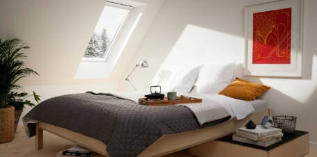 Schlafzimmer im Spitzboden mit weißen Wänden, Vollholzmöbeln, Holzdielen und rotem Gemälde an der Wand | VELUX Magazin