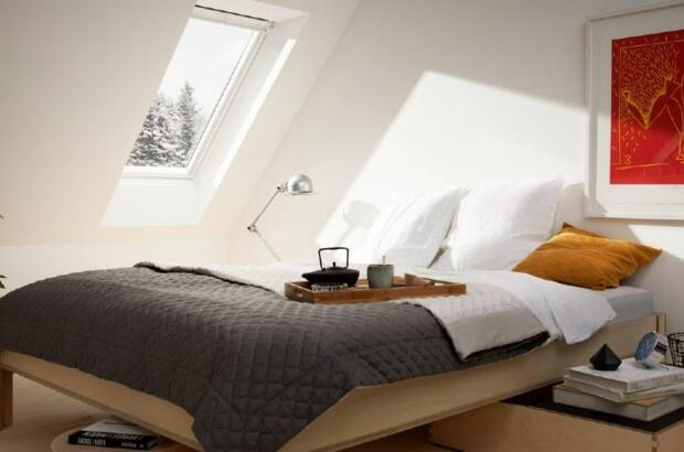 Schlafzimmer im Spitzboden mit weißen Wänden, Vollholzmöbeln, Holzdielen und rotem Gemälde an der Wand | VELUX Magazin