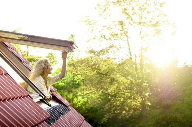 Frau blickt aus ihrem Dachfenster ins Grüne und tankt Tageslicht | VELUX Magazin