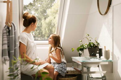 Mutter sitzt mit ihrer Tochter am Dachfenster und genießt das Tageslicht | VELUX Magazin