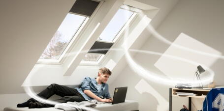 Junger Mann liegt auf dem Bett vor Dachfenstern | VELUX Magazin